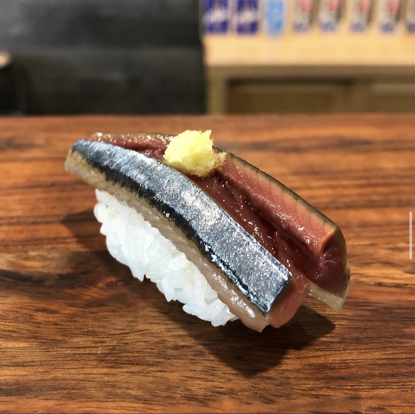 Taka’s 木质吧台上的 Sanma 秋刀鱼握寿司，保留银色鱼皮，配有少许点缀