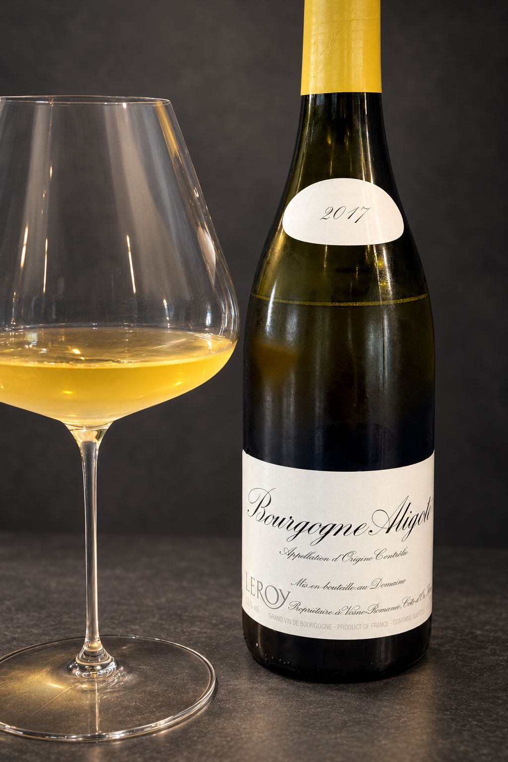 炭灰色背景前的Leroy Bourgogne Aligoté 2017酒瓶与一杯白葡萄酒