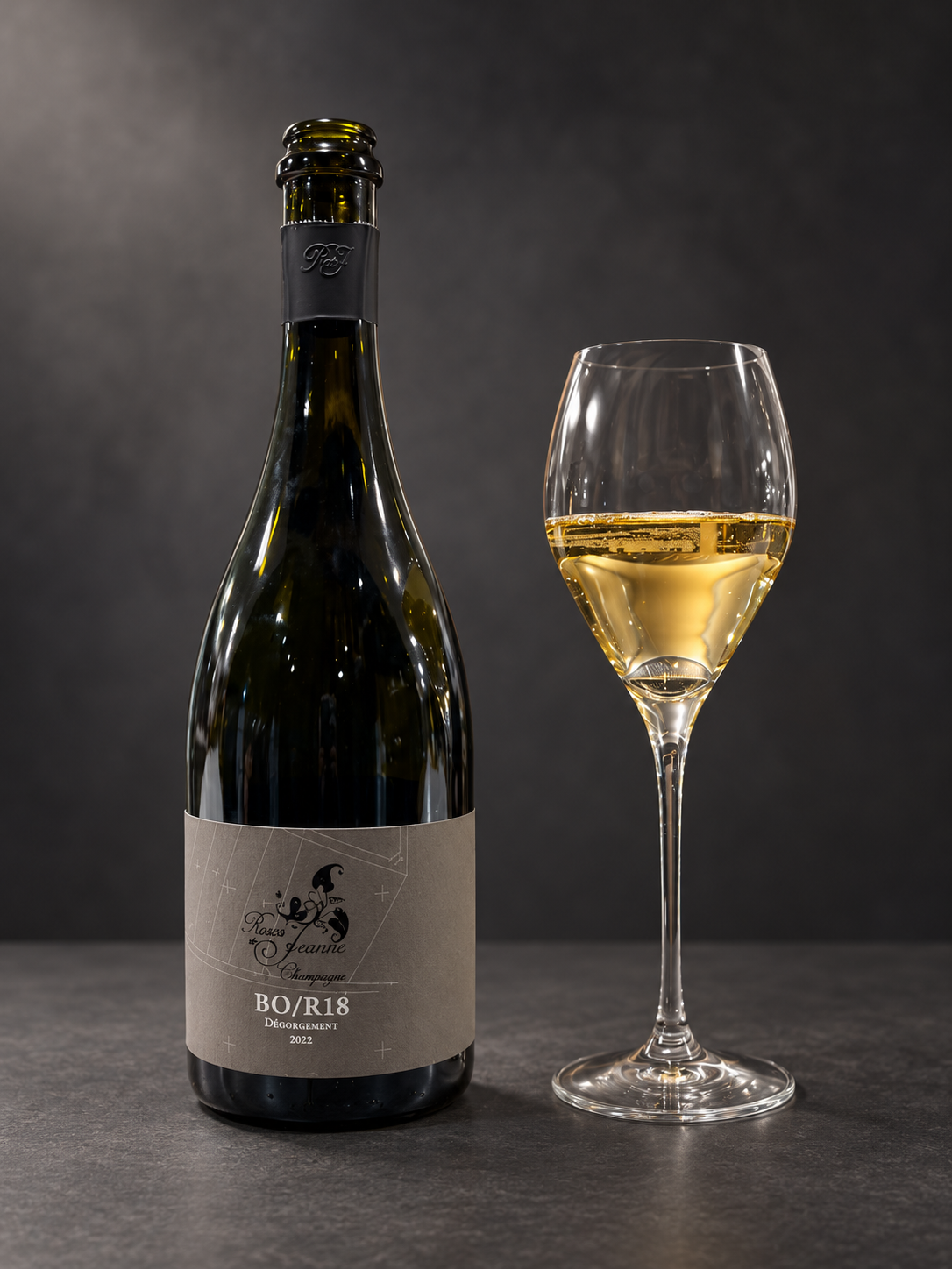 Roses de Jeanne BO/R18 香槟酒瓶与酒杯,置于炭灰色背景前,酒标注明2022年除渣