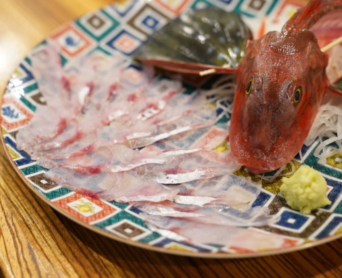 薄切 Hōbō(ホウボウ)刺身在花纹盘上扇形排列,旁边摆着鱼头